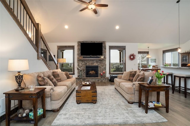 living area featuring wood finished floors, ceiling fan, a fireplace, stairs, and vaulted ceiling