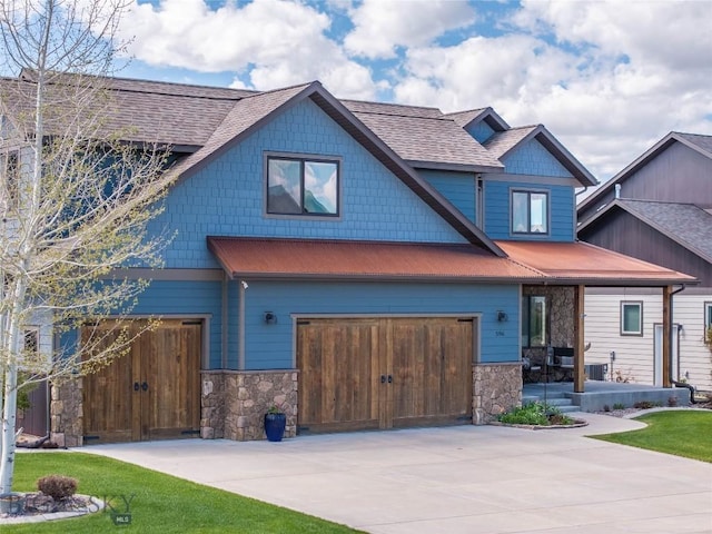 craftsman-style home with driveway, stone siding, an attached garage, and a front lawn