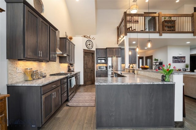 kitchen featuring appliances with stainless steel finishes, a towering ceiling, wood finished floors, dark brown cabinetry, and a sink