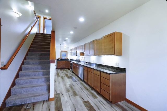 kitchen with stainless steel dishwasher, a sink, light wood finished floors, brown cabinetry, and dark stone counters