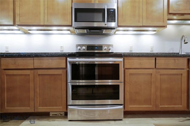 kitchen with appliances with stainless steel finishes, dark stone countertops, and light wood finished floors