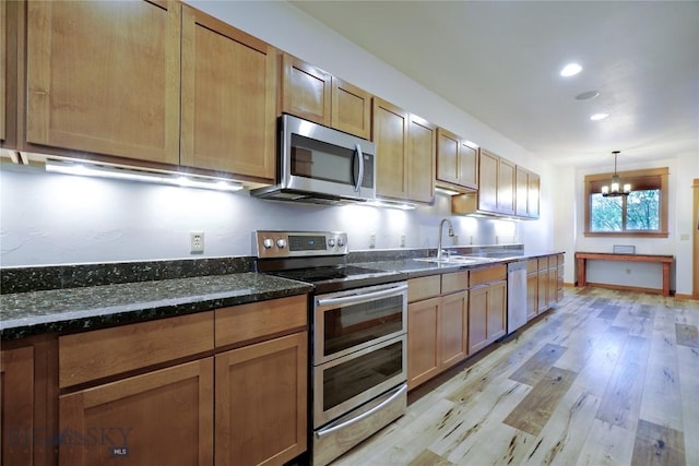 kitchen featuring appliances with stainless steel finishes, a sink, a chandelier, light wood-type flooring, and dark stone countertops