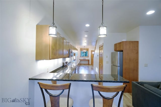 kitchen featuring appliances with stainless steel finishes, a peninsula, a sink, a breakfast bar area, and recessed lighting