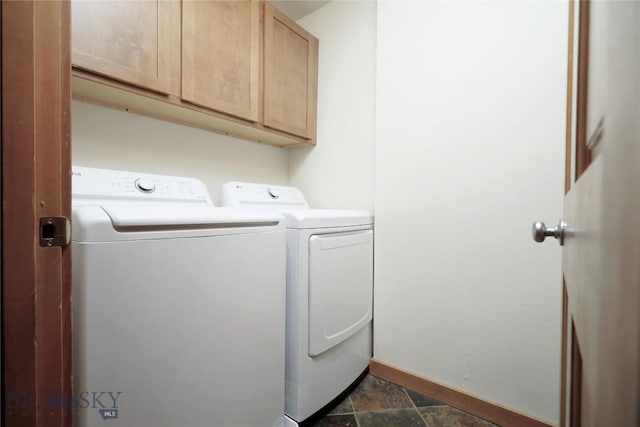 clothes washing area featuring washer and dryer, cabinet space, baseboards, and dark stone finish flooring