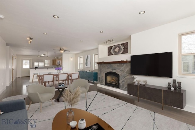 living room with wood finished floors, a stone fireplace, baseboards, ceiling fan, and recessed lighting