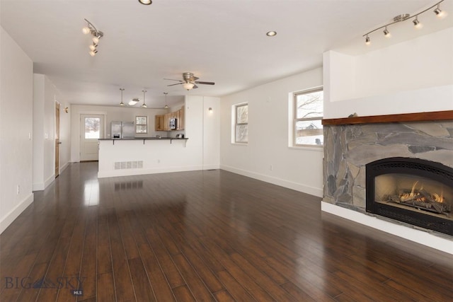 unfurnished living room with ceiling fan, rail lighting, baseboards, and a stone fireplace