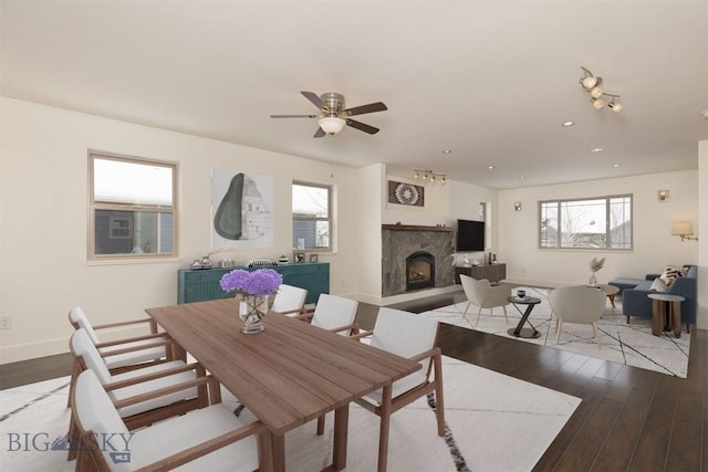 dining space featuring wood finished floors, baseboards, a fireplace with raised hearth, ceiling fan, and recessed lighting