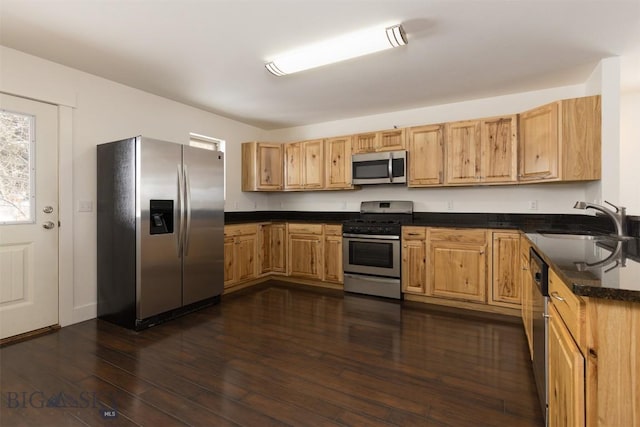 kitchen with appliances with stainless steel finishes, a sink, dark countertops, and dark wood-type flooring