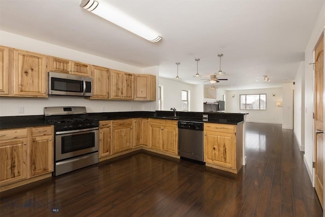 kitchen featuring appliances with stainless steel finishes, a peninsula, a sink, and dark countertops