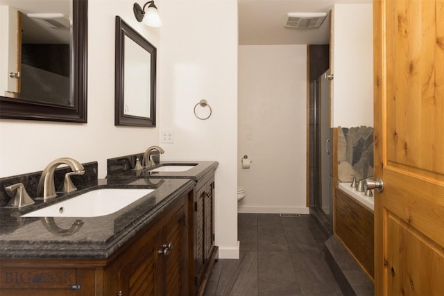 bathroom featuring a stall shower, toilet, double vanity, baseboards, and tile patterned flooring