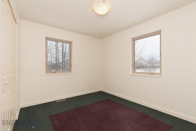 spare room featuring dark carpet, plenty of natural light, and baseboards
