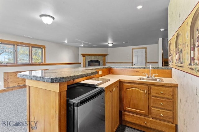 3450 W Hollyhock Dr, Belgrade, MT 59714 - kitchen with a sink, refrigerator, a peninsula, a fireplace with raised hearth, and brown cabinetry