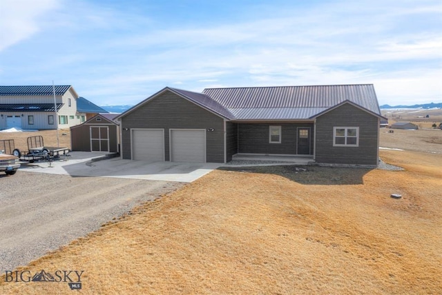 view of front of home with gravel driveway, a garage, metal roof, and a shed