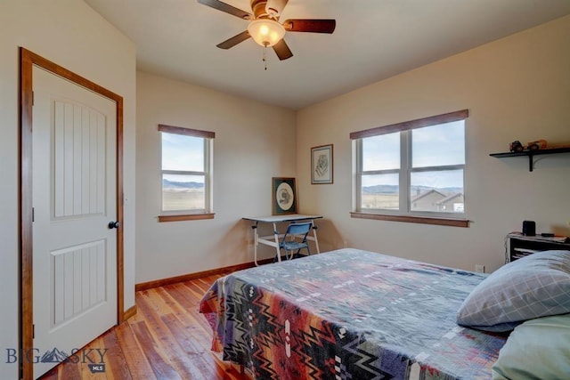 bedroom featuring multiple windows, light wood finished floors, baseboards, and ceiling fan