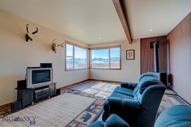 living area featuring beamed ceiling, a wood stove, baseboards, and wood finished floors