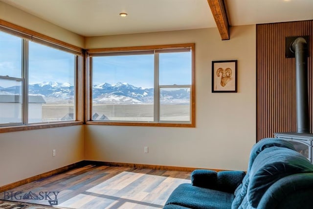 sitting room with a wood stove, healthy amount of natural light, wood finished floors, a mountain view, and beamed ceiling