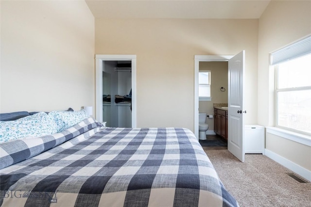 bedroom with multiple windows, light colored carpet, baseboards, and ensuite bathroom