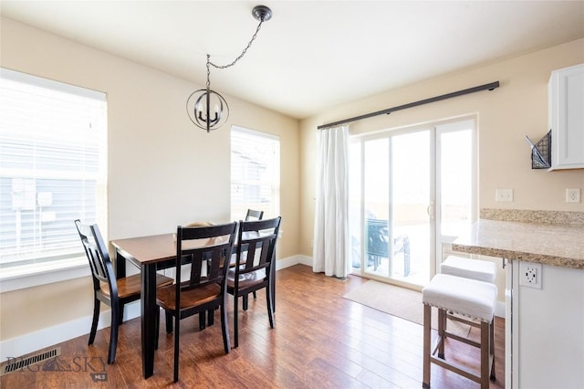 dining space with dark wood-type flooring, a chandelier, and baseboards