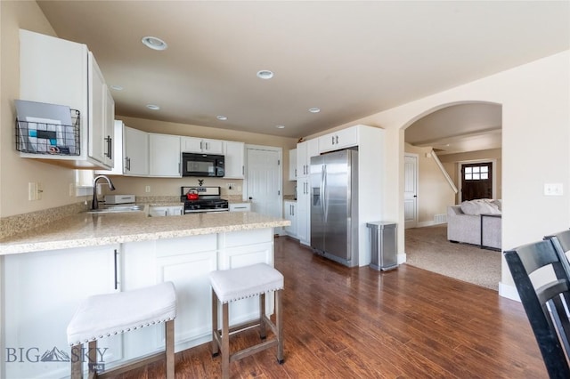 kitchen with appliances with stainless steel finishes, a sink, a peninsula, arched walkways, and recessed lighting