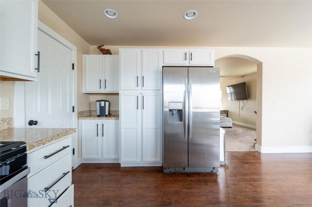kitchen with stainless steel fridge, arched walkways, white cabinetry, light stone counters, and recessed lighting