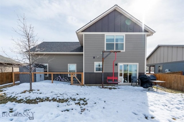 snow covered property with fence and board and batten siding