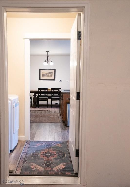 hall with washing machine and clothes dryer, wood finished floors, and a chandelier