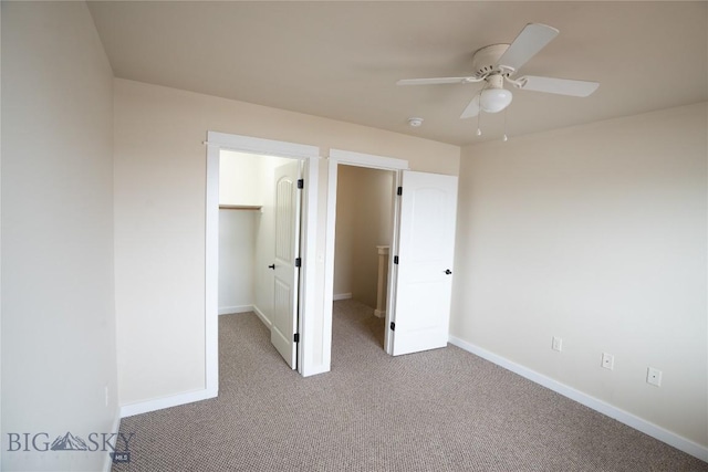 unfurnished bedroom featuring carpet, a walk in closet, baseboards, and ceiling fan
