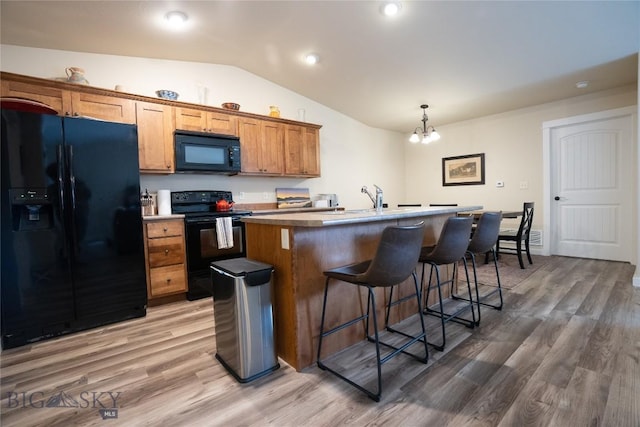 kitchen featuring black appliances, lofted ceiling, a kitchen island with sink, a kitchen breakfast bar, and brown cabinetry