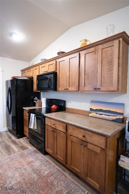 kitchen featuring black appliances, vaulted ceiling, light wood-style floors, and brown cabinets