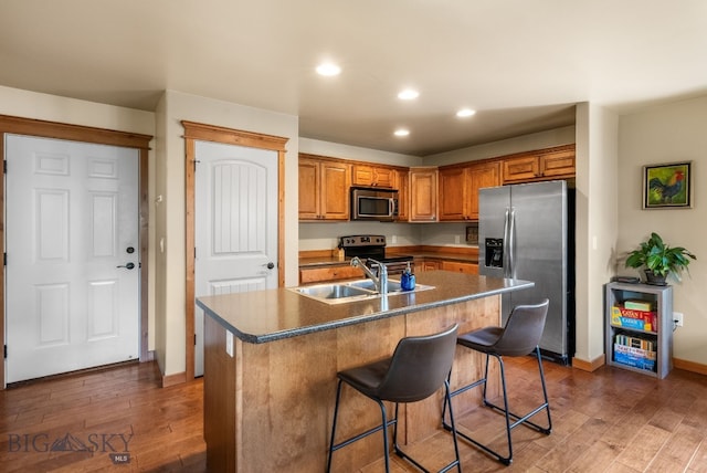 kitchen with stainless steel appliances, a sink, recessed lighting, wood finished floors, and baseboards