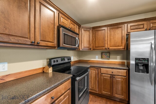 kitchen with appliances with stainless steel finishes, dark countertops, and brown cabinets