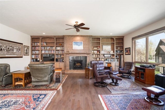 living area with ceiling fan, a tiled fireplace, wood finished floors, recessed lighting, and built in shelves