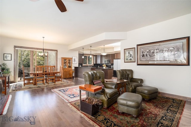 living area featuring dark wood-style flooring, ceiling fan, a chandelier, and baseboards