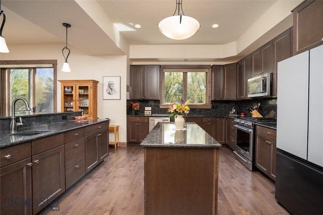 kitchen with stainless steel appliances, a sink, backsplash, a kitchen island, and dark stone countertops