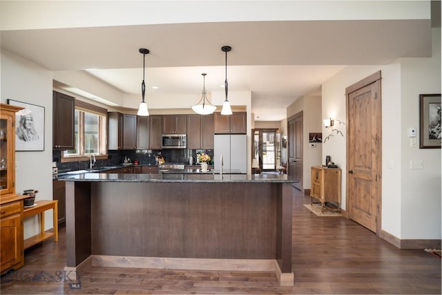 kitchen featuring stainless steel appliances, dark wood-type flooring, dark brown cabinets, backsplash, and a center island