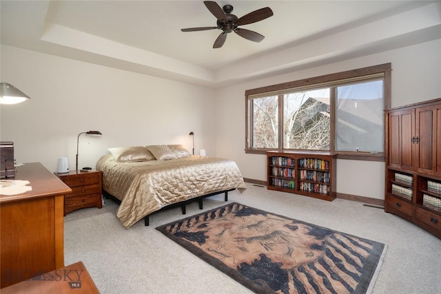 bedroom featuring light carpet, a tray ceiling, baseboards, and ceiling fan