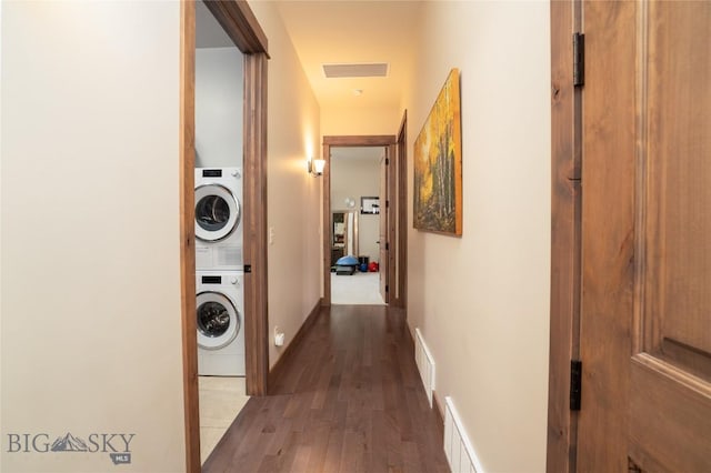 hallway with stacked washer and clothes dryer, wood finished floors, and baseboards