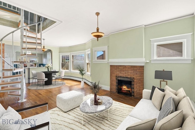 living area featuring stairway, wood finished floors, a brick fireplace, ornamental molding, and baseboard heating