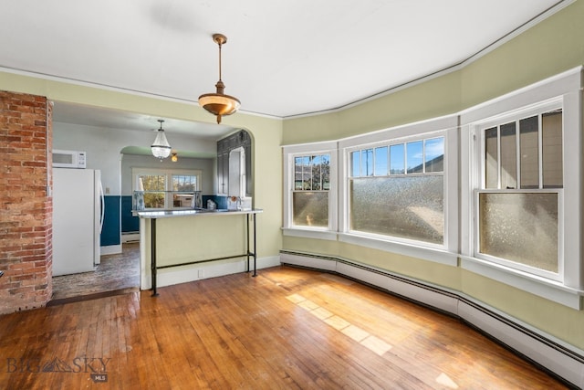 kitchen with white appliances, baseboard heating, hardwood / wood-style flooring, arched walkways, and hanging light fixtures