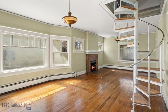 unfurnished living room featuring baseboard heating, stairs, and hardwood / wood-style floors