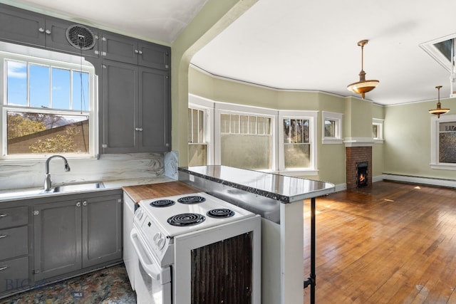 kitchen with white range with electric cooktop, gray cabinetry, a sink, a peninsula, and a brick fireplace