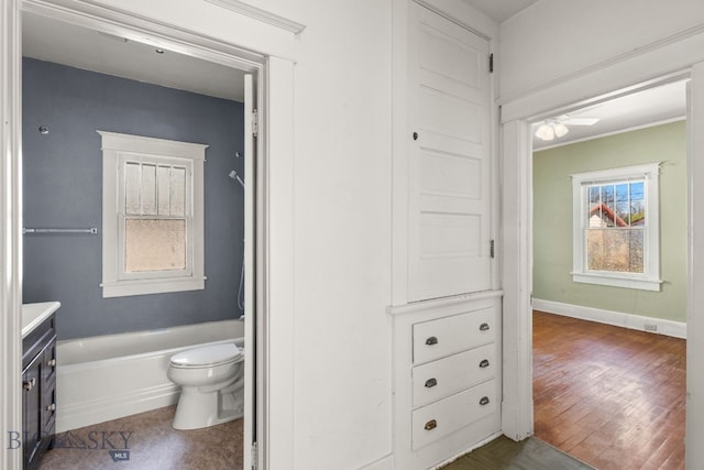 full bathroom with toilet, a tub, vanity, wood finished floors, and baseboards