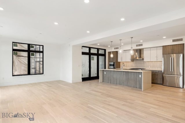 kitchen featuring freestanding refrigerator, wall chimney range hood, modern cabinets, open floor plan, and light countertops