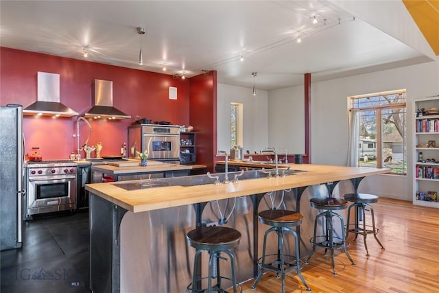 kitchen featuring wood counters, wall chimney exhaust hood, appliances with stainless steel finishes, and a large island