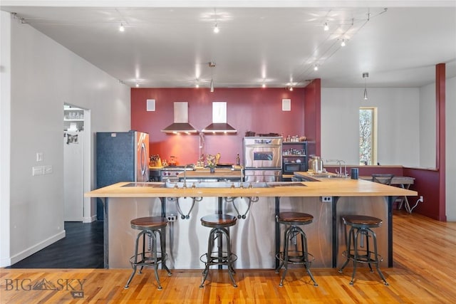 kitchen featuring wall chimney exhaust hood, butcher block countertops, appliances with stainless steel finishes, and a sink