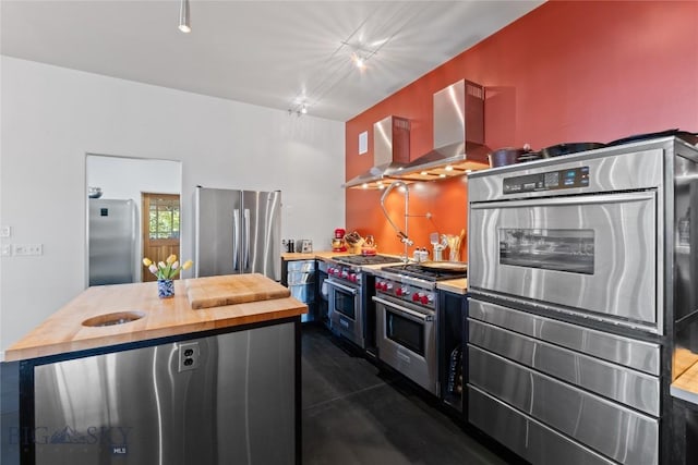 kitchen with stainless steel appliances, wood counters, wall chimney exhaust hood, and a kitchen island