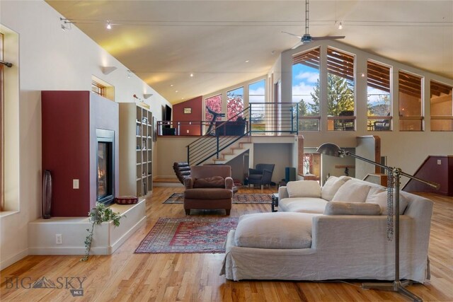 living room with a ceiling fan, stairway, wood finished floors, baseboards, and high vaulted ceiling