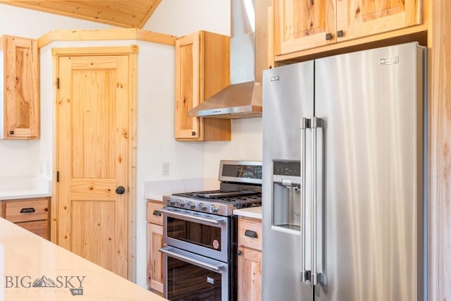 kitchen featuring stainless steel appliances, wall chimney exhaust hood, light countertops, light brown cabinetry, and vaulted ceiling