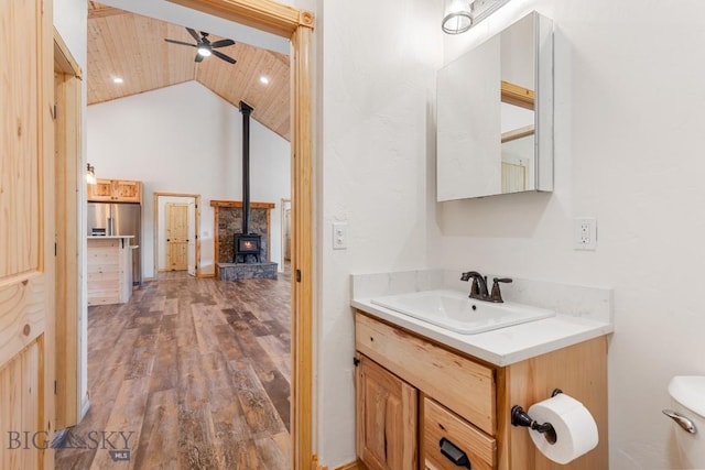 bathroom with a wood stove, lofted ceiling, wood finished floors, a ceiling fan, and vanity