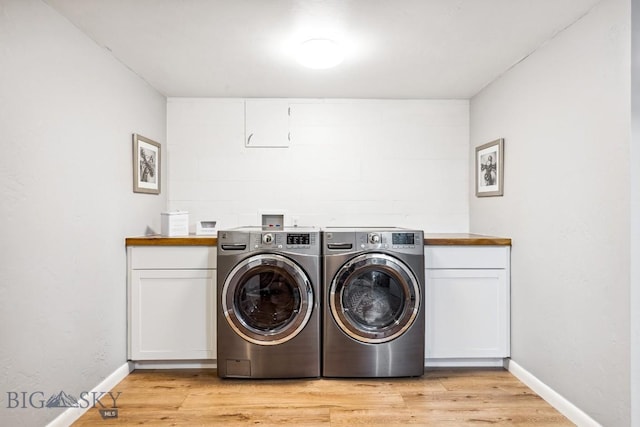 clothes washing area with independent washer and dryer, cabinet space, light wood finished floors, and baseboards